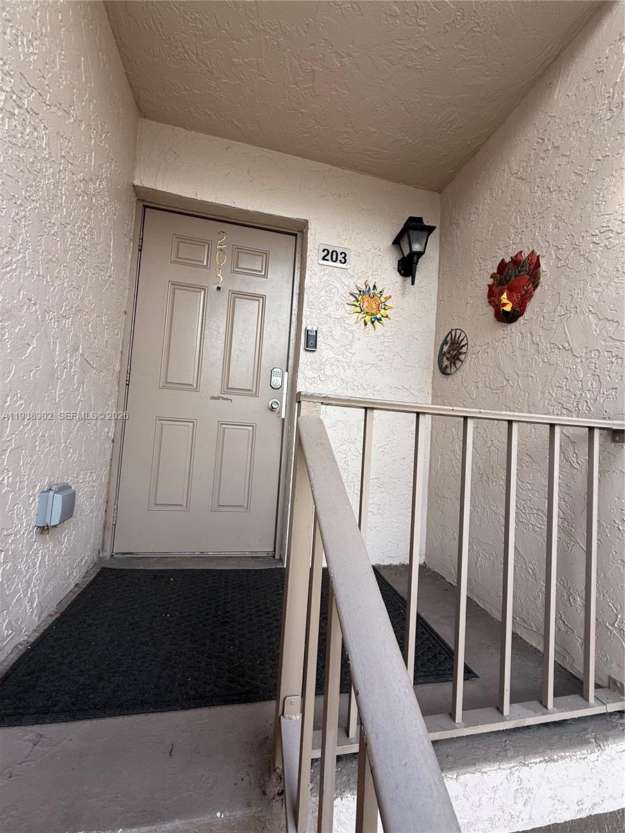 An exterior view of a residential apartment entrance with a tan door numbered 203 — 1040 NW 80th Ave # 203, Margate FL 33063, MARGATE, FL