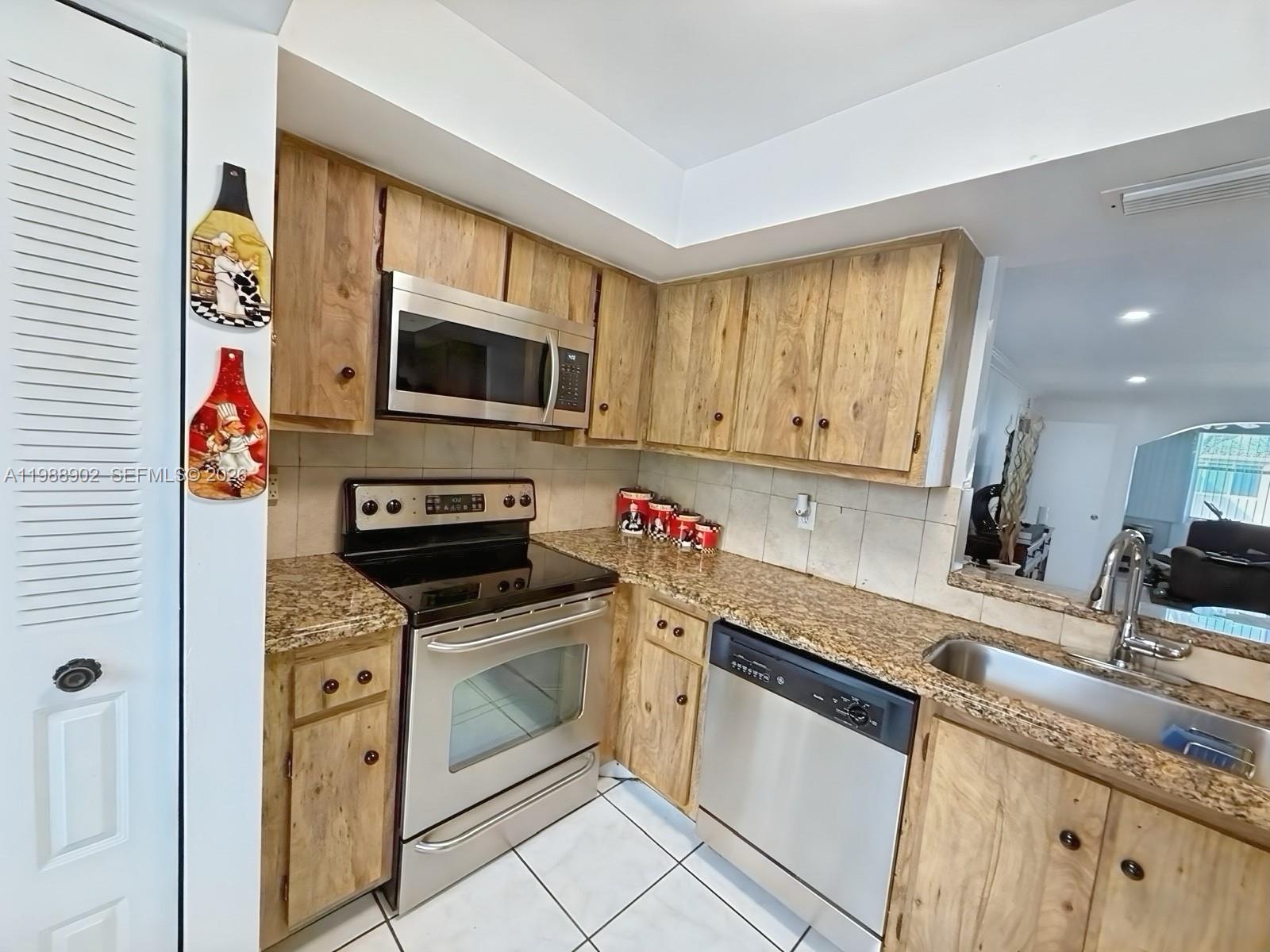A kitchen features wood cabinets, granite countertops, stainless steel appliances, and white tile flooring — 1040 NW 80th Ave # 203, Margate FL 33063, MARGATE, FL