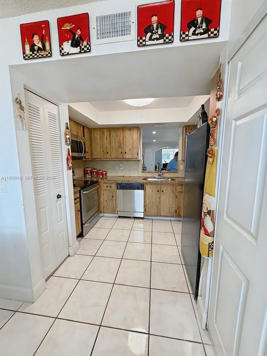 A kitchen features wood cabinets, granite countertops, stainless steel appliances, and white tiled flooring — 1040 NW 80th Ave # 203, Margate FL 33063, MARGATE, FL