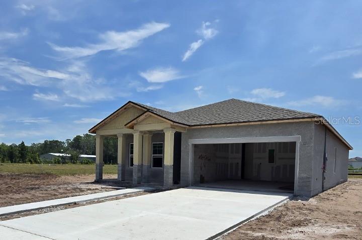 A newly constructed single-story house with a concrete driveway, unfinished exterior, and an open garage — 1623 CANE BAMBOO DRIVE, ST CLOUD, FL