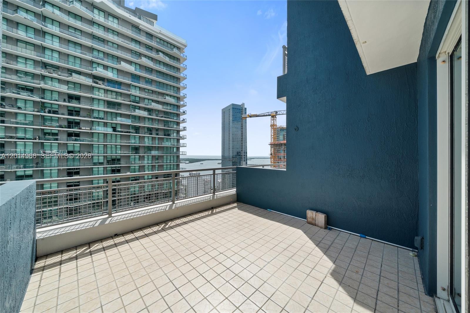 A balcony with light-colored tile flooring overlooks a bay and nearby high-rise buildings — 60 SW 13th St # 4008, Miami FL 33130, MIAMI, FL