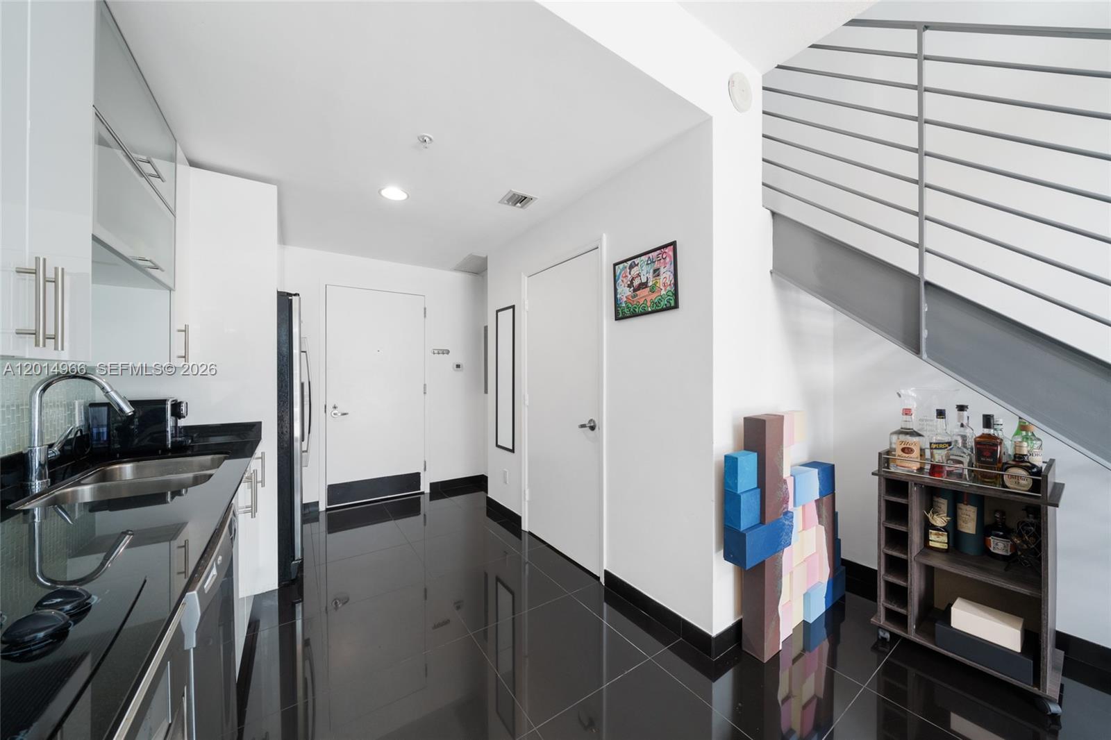 A modern kitchen with black countertops and tile flooring features a staircase and bar cart — 60 SW 13th St # 4008, Miami FL 33130, MIAMI, FL