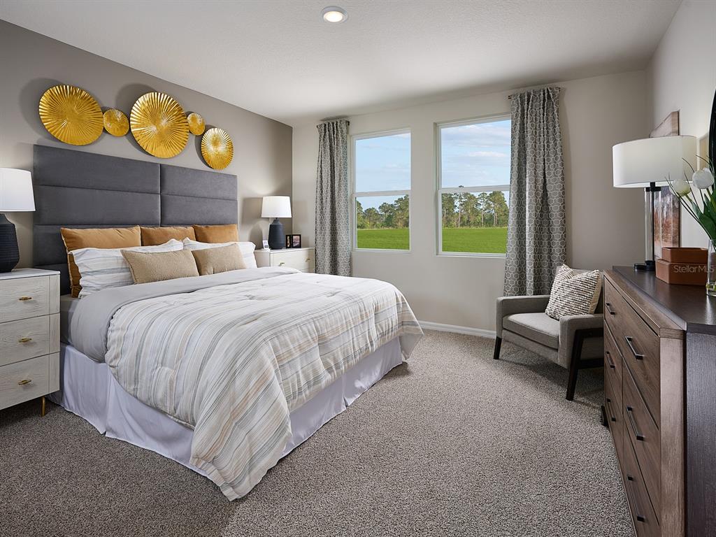 A bedroom features a gray upholstered headboard, gold wall art, and a view of trees — 1533 BREKEY WAY, ZEPHYRHILLS, FL