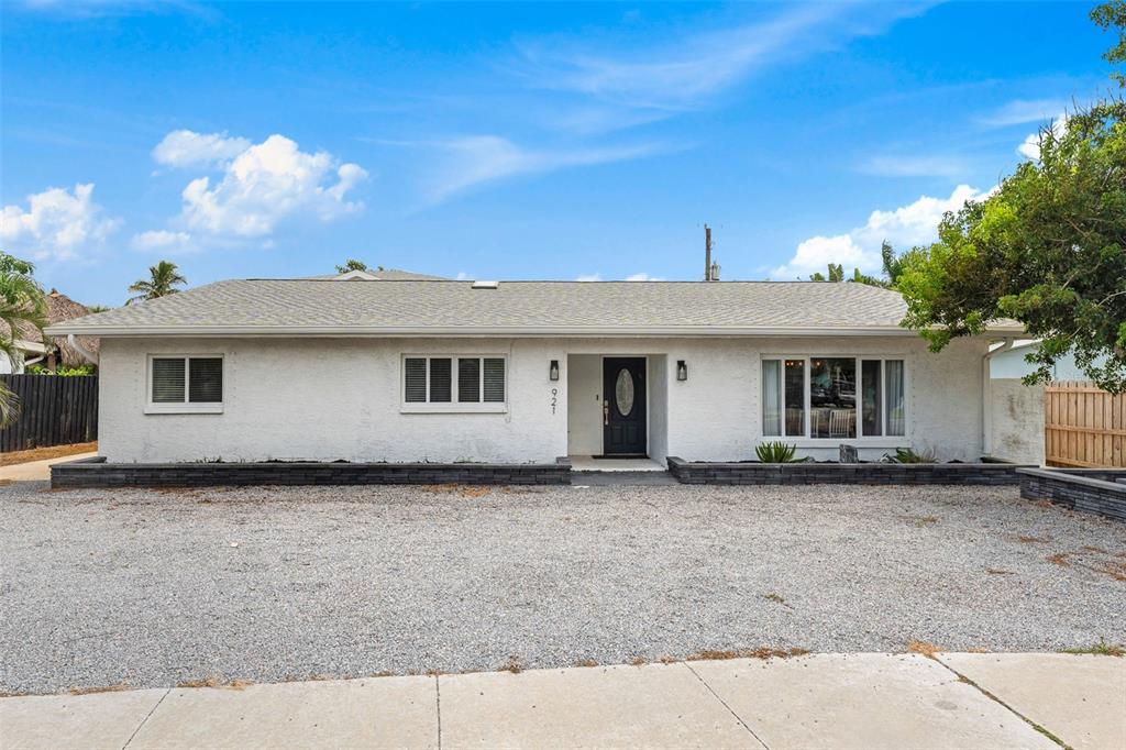 A single-story white house with a gravel driveway and a dark-colored front door — 921 S ORLANDO AVENUE, COCOA BEACH, FL