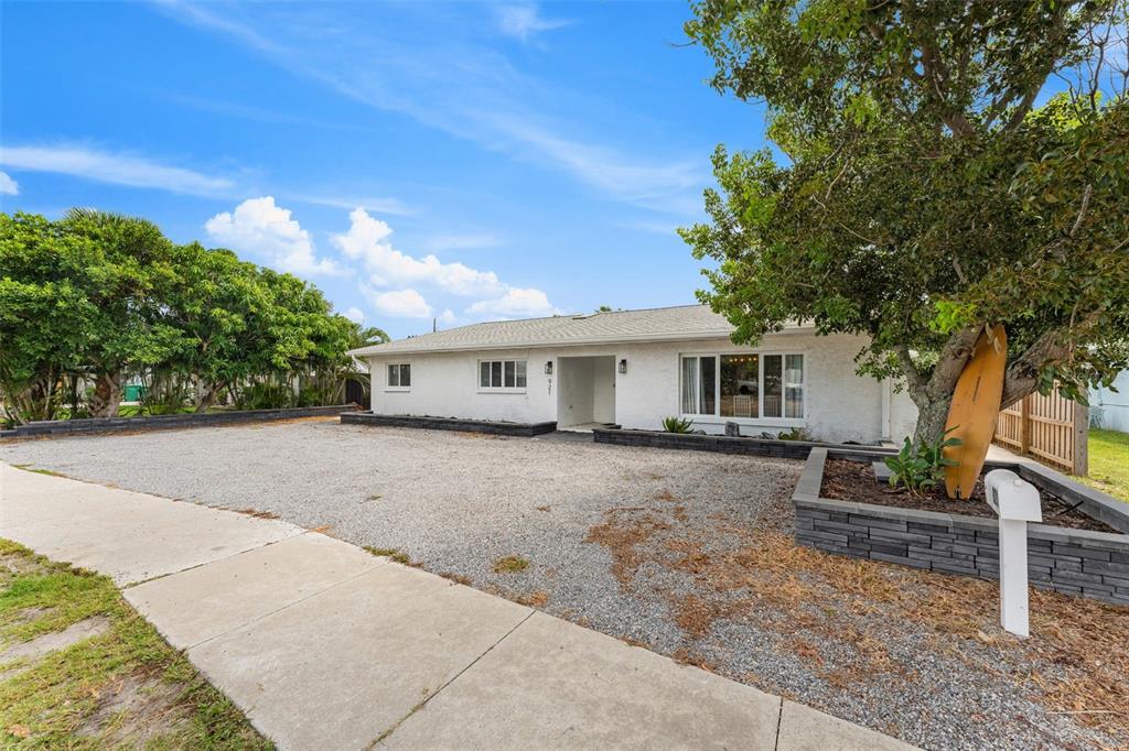 A white single-story house features a gravel driveway, a large tree, and stone planter walls — 921 S ORLANDO AVENUE, COCOA BEACH, FL
