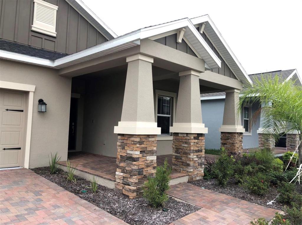 A house exterior featuring a covered porch with stone-based columns and a brick paver walkway — 10229 LOVEGRASS LANE, ORLANDO, FL
