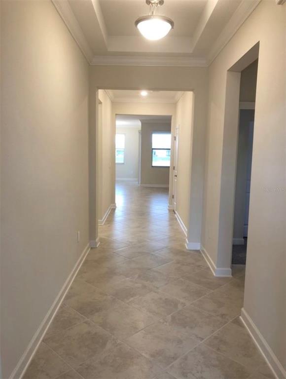 A hallway with beige walls, tile flooring, and a tray ceiling with a light fixture — 10229 LOVEGRASS LANE, ORLANDO, FL