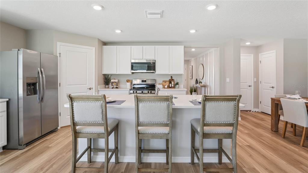 A kitchen features a white island with three stools, stainless steel appliances, and wood flooring — 5767 SW 130TH LANE, OCALA, FL