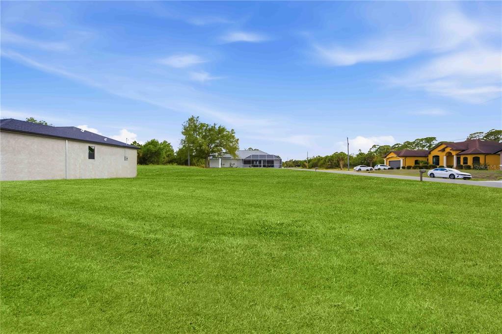 A large, grassy vacant lot sits in front of suburban houses under a blue sky — ATTALLA AVENUE, NORTH PORT, FL