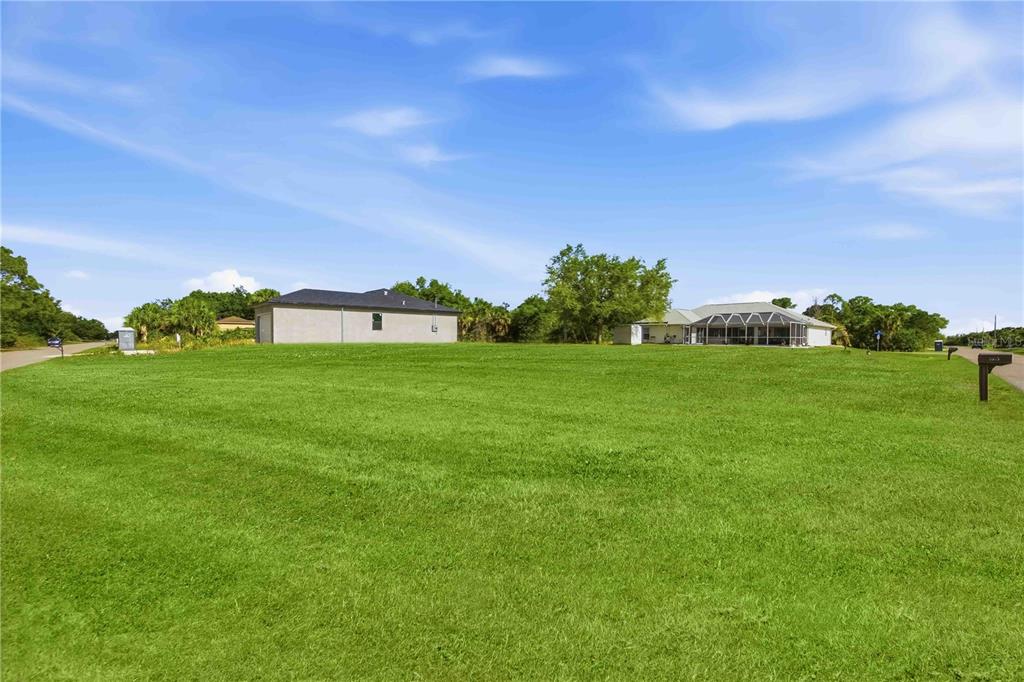 A large, grassy vacant lot sits in front of two residential houses under a blue sky — ATTALLA AVENUE, NORTH PORT, FL