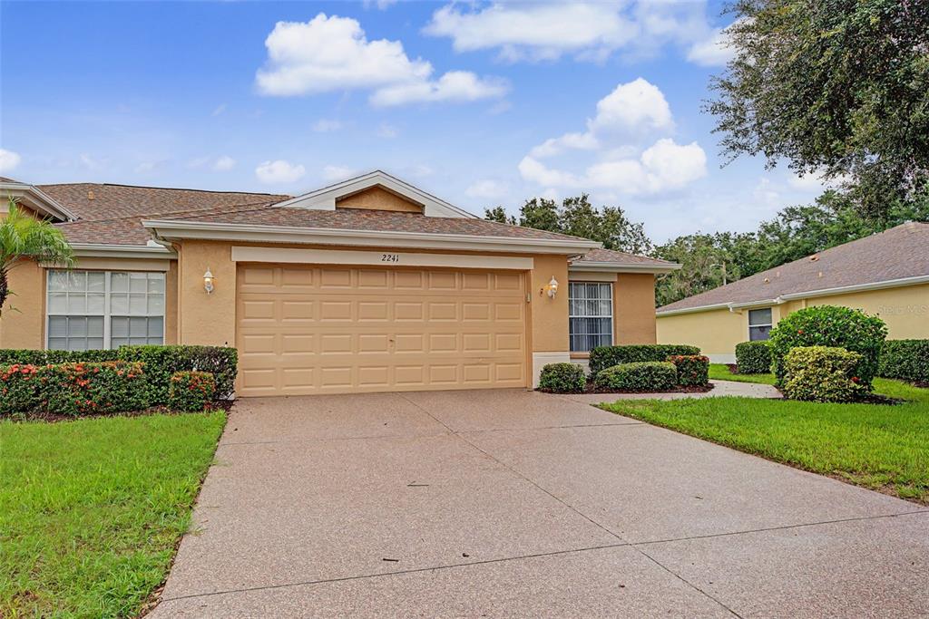 A tan single-story house with a two-car garage and a concrete driveway — 2241 WORTHINGTON GREENS DRIVE, SUN CITY CENTER, FL