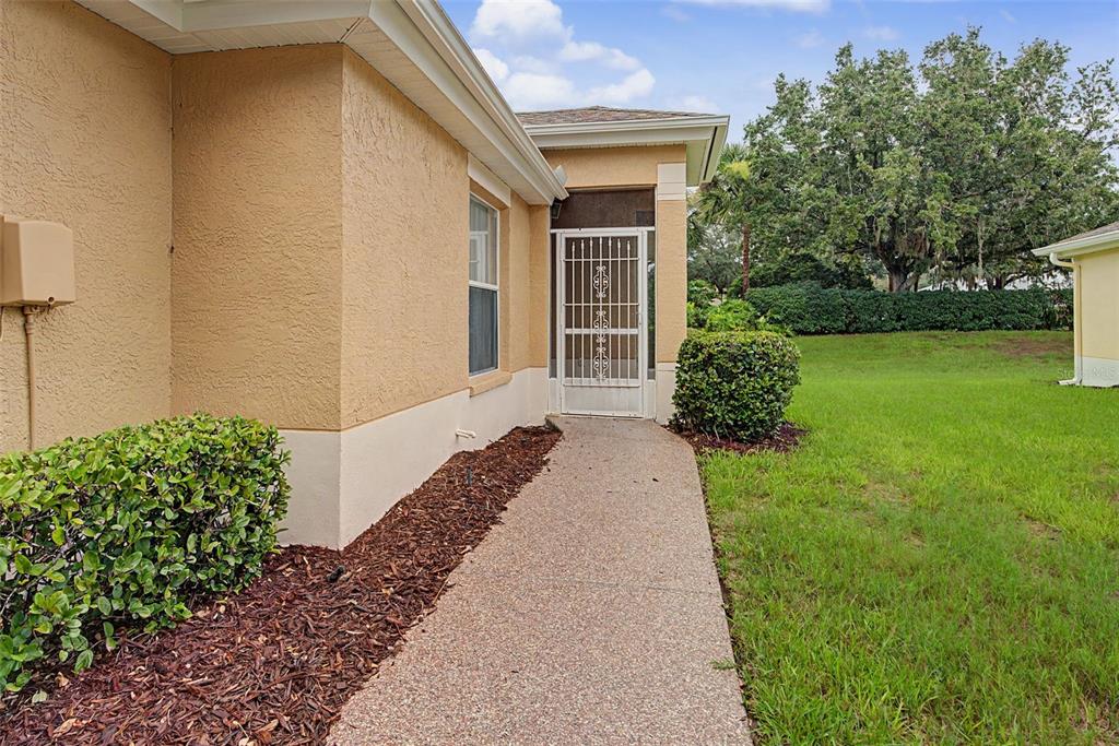 A concrete walkway leads to a screened entryway on the side of a stucco house — 2241 WORTHINGTON GREENS DRIVE, SUN CITY CENTER, FL