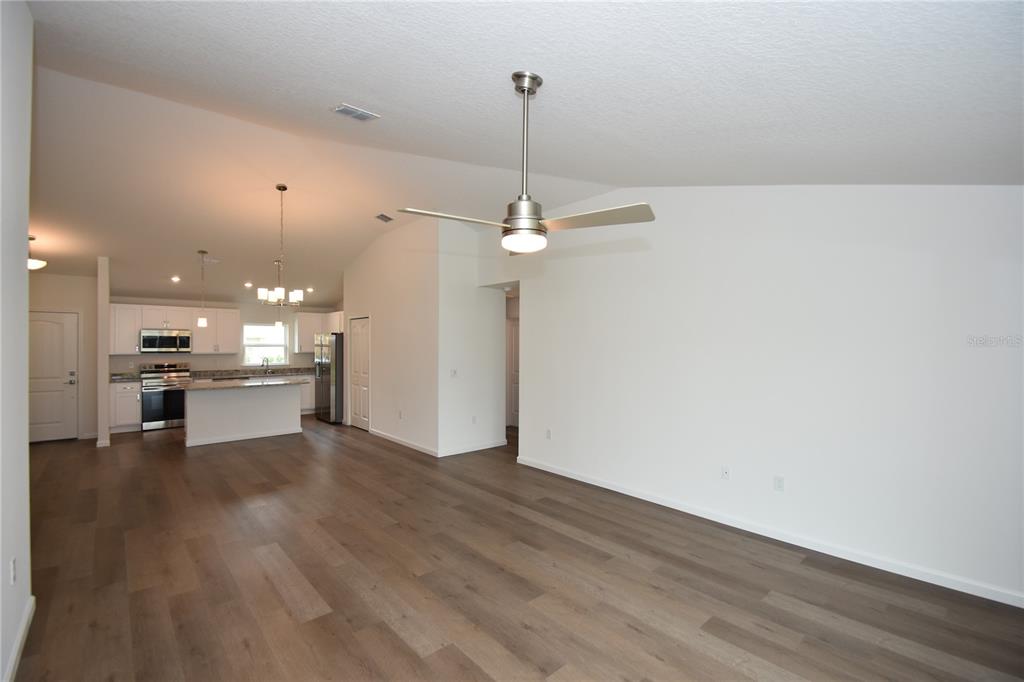 An open-concept living area features wood-look flooring, a vaulted ceiling with a fan, and a kitchen — 14 POWDER LANE, PALM COAST, FL
