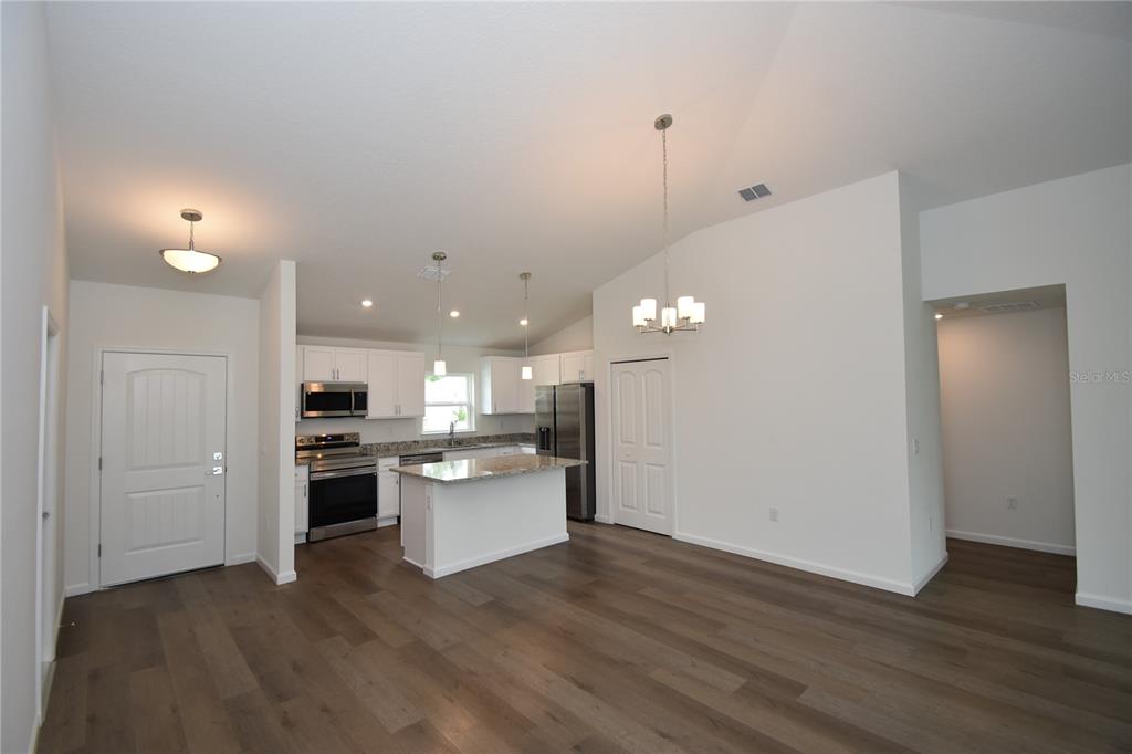 An open-concept kitchen features white cabinets, granite countertops, stainless steel appliances, and wood-look flooring — 14 POWDER LANE, PALM COAST, FL