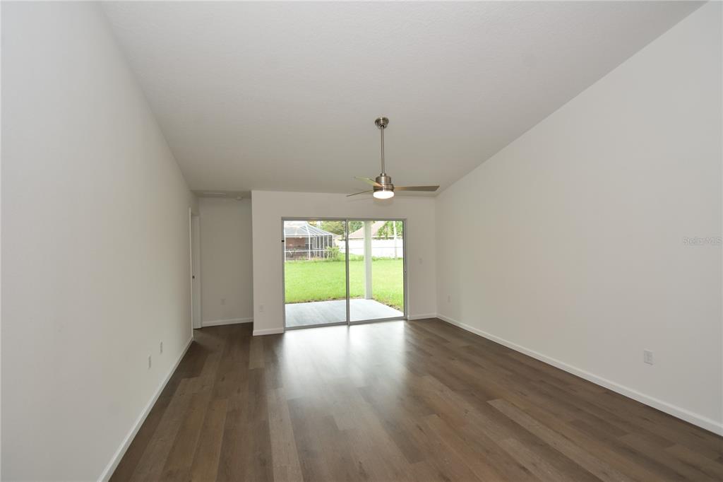 An empty living room features wood-look flooring, a ceiling fan, and sliding glass doors to a patio — 14 POWDER LANE, PALM COAST, FL