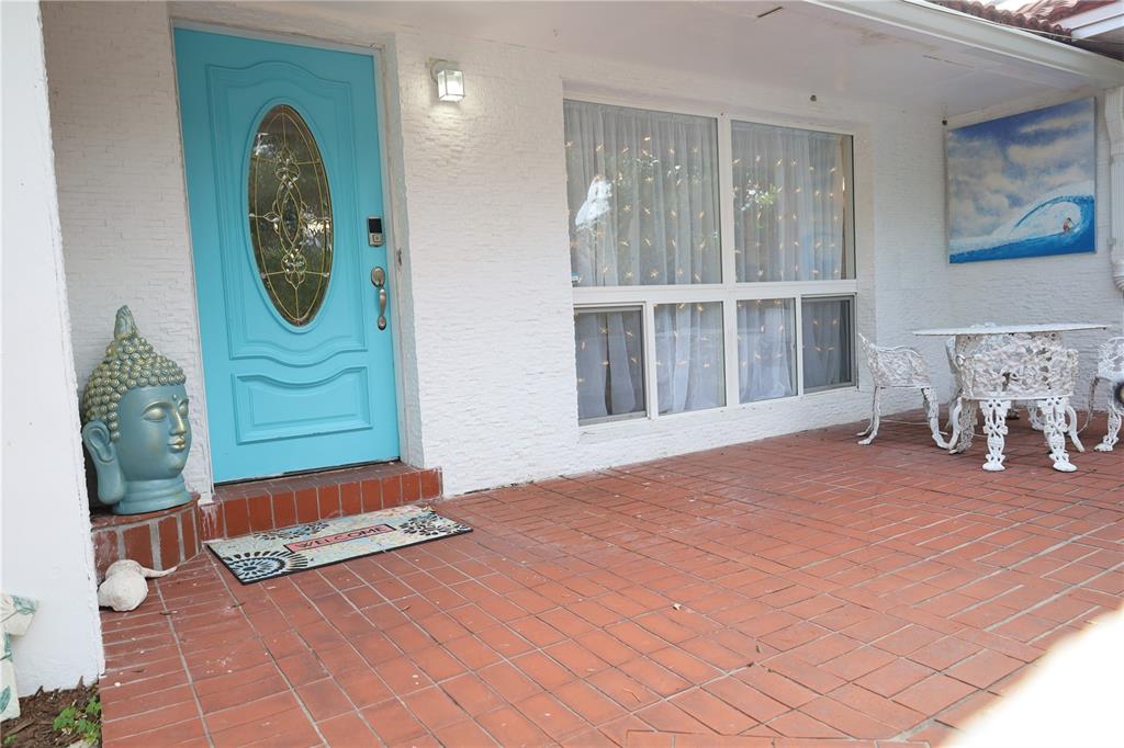 A white house exterior features a bright blue front door, a red brick patio, and furniture — 7716 DARTMOUTH AVENUE N, ST PETERSBURG, FL