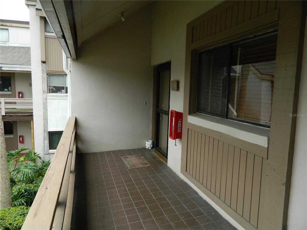 A tiled outdoor balcony features a wooden railing, a glass door, and a wall-mounted fire extinguisher — 266 ORIENTA POINT STREET, ALTAMONTE SPRINGS, FL