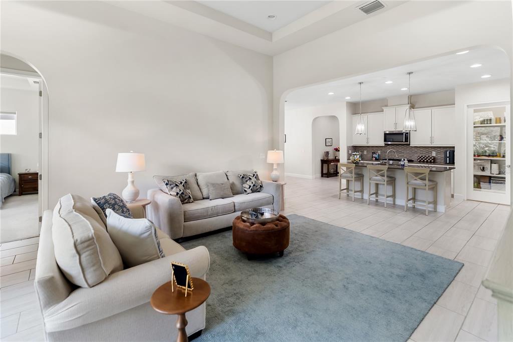A living room with light-colored furniture and a blue rug opens to a kitchen area — 2312 STARWOOD COURT, BRADENTON, FL
