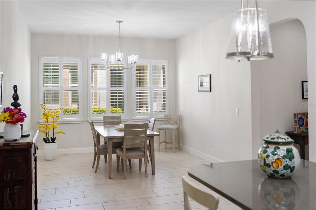 A dining area features a wooden table, four chairs, plantation shutters, and a chandelier — 2312 STARWOOD COURT, BRADENTON, FL