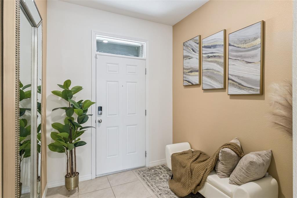 An entryway features a white front door, a tall potted plant, a mirror, and a bench — 1707 WOODEN STREET, DAVENPORT, FL
