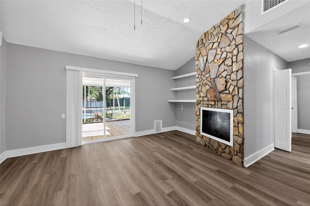 A living room features wood-look flooring, a stone fireplace, built-in shelves, and sliding glass doors — 1150 52ND STREET, SARASOTA, FL