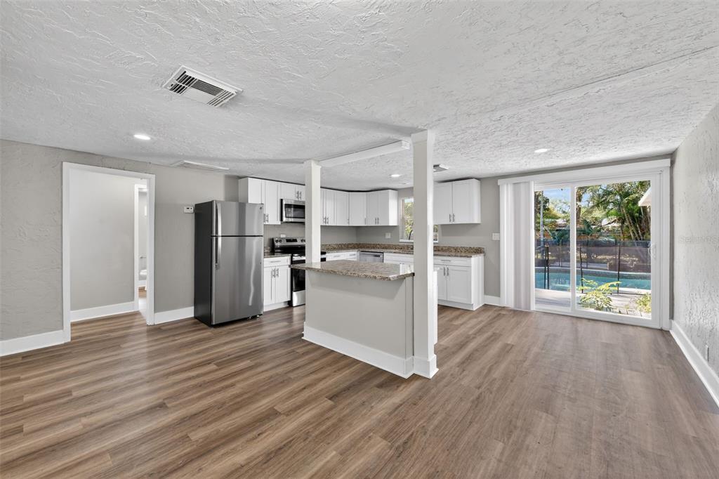 A kitchen with white cabinets, granite countertops, and stainless steel appliances opens to a living area — 1150 52ND STREET, SARASOTA, FL