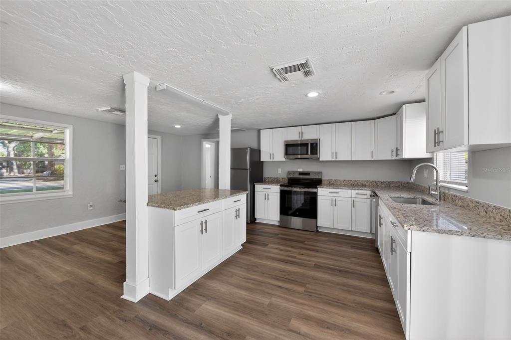 A kitchen features white cabinets, granite countertops, stainless steel appliances, and wood-look flooring — 1150 52ND STREET, SARASOTA, FL