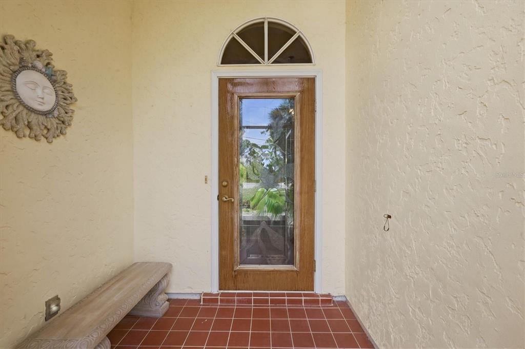 A front entryway features a glass-paneled wooden door, a sun wall decoration, and tiled flooring — 5534 DAVID BOULEVARD, PORT CHARLOTTE, FL