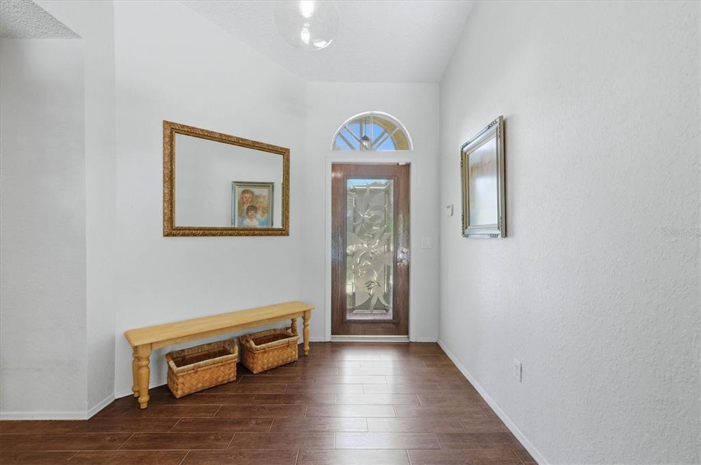 An entryway features wood-look tile flooring, a wooden bench with baskets, and a glass-paneled door — 5534 DAVID BOULEVARD, PORT CHARLOTTE, FL