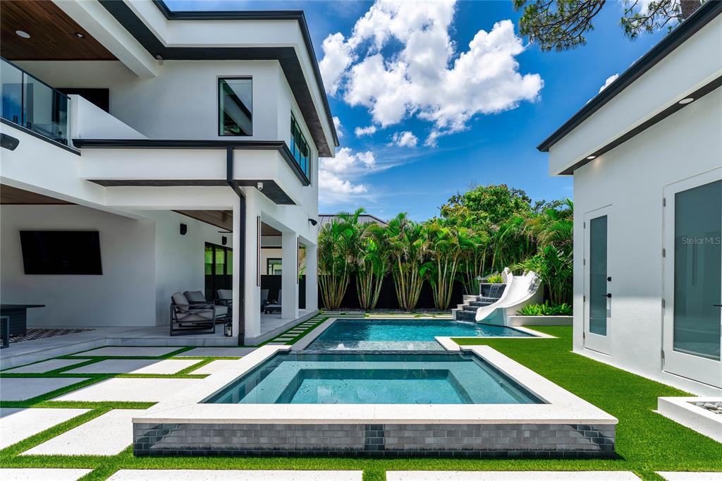 A modern backyard features a swimming pool, a raised spa, and a white water slide — 5002 W POE AVENUE, TAMPA, FL