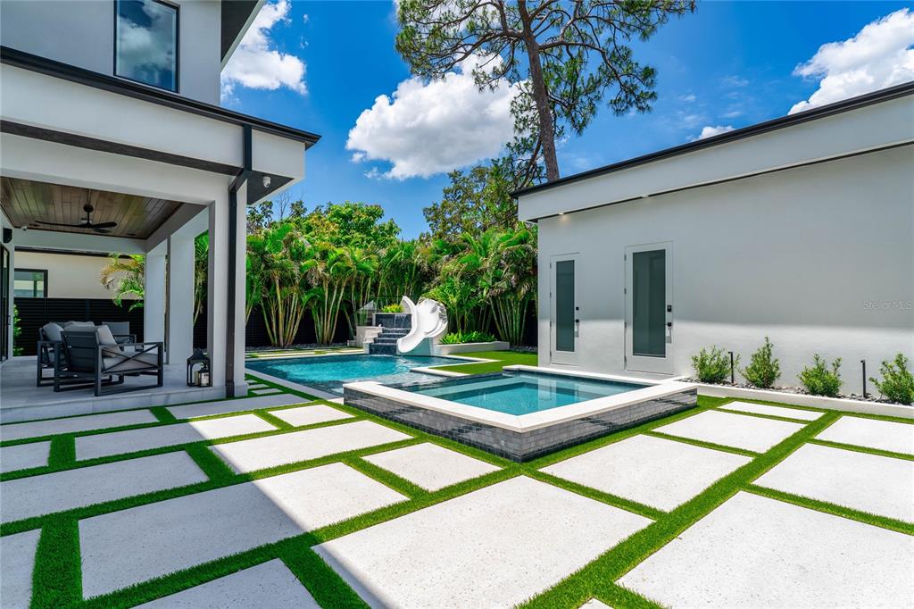 A modern backyard features a pool, a raised spa, and a patio with grass pavers — 5002 W POE AVENUE, TAMPA, FL