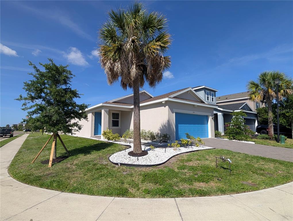 A single-story house with a blue garage door, a palm tree, and a landscaped front yard — 5763 BUNGALOW GROVE COURT, PALMETTO, FL