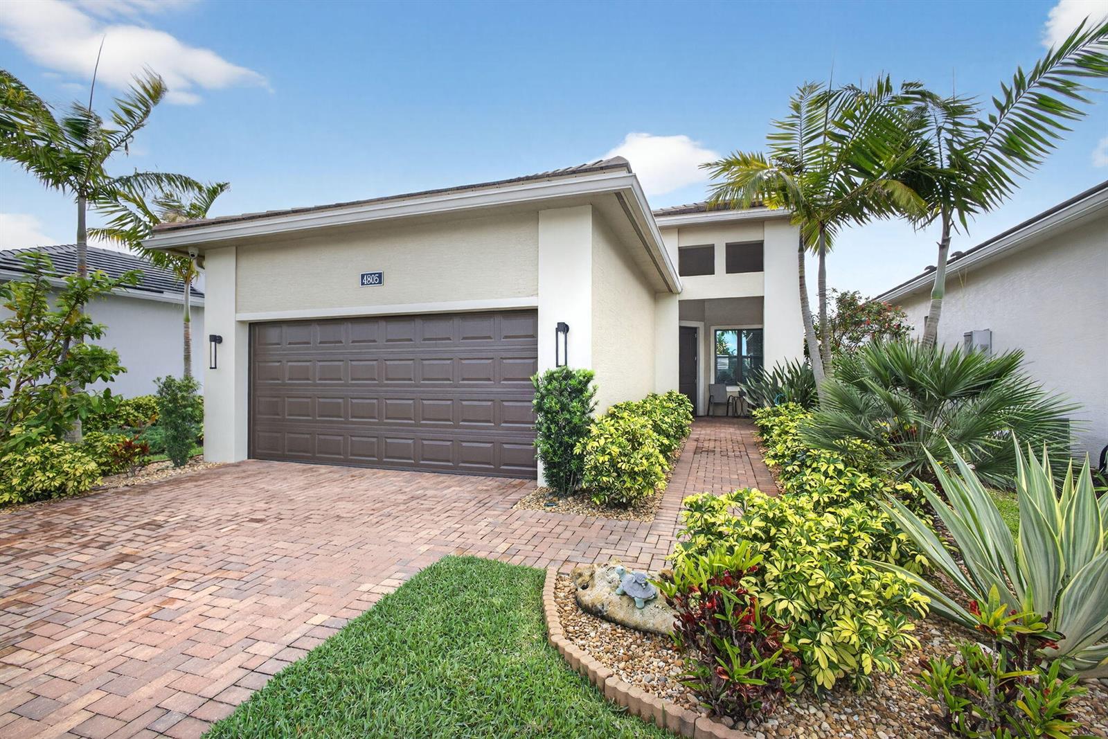 A single-story house with a brown garage door, brick driveway, and tropical landscaping — 4805 Saint Armands Way, Westlake FL 33470, WESTLAKE, FL
