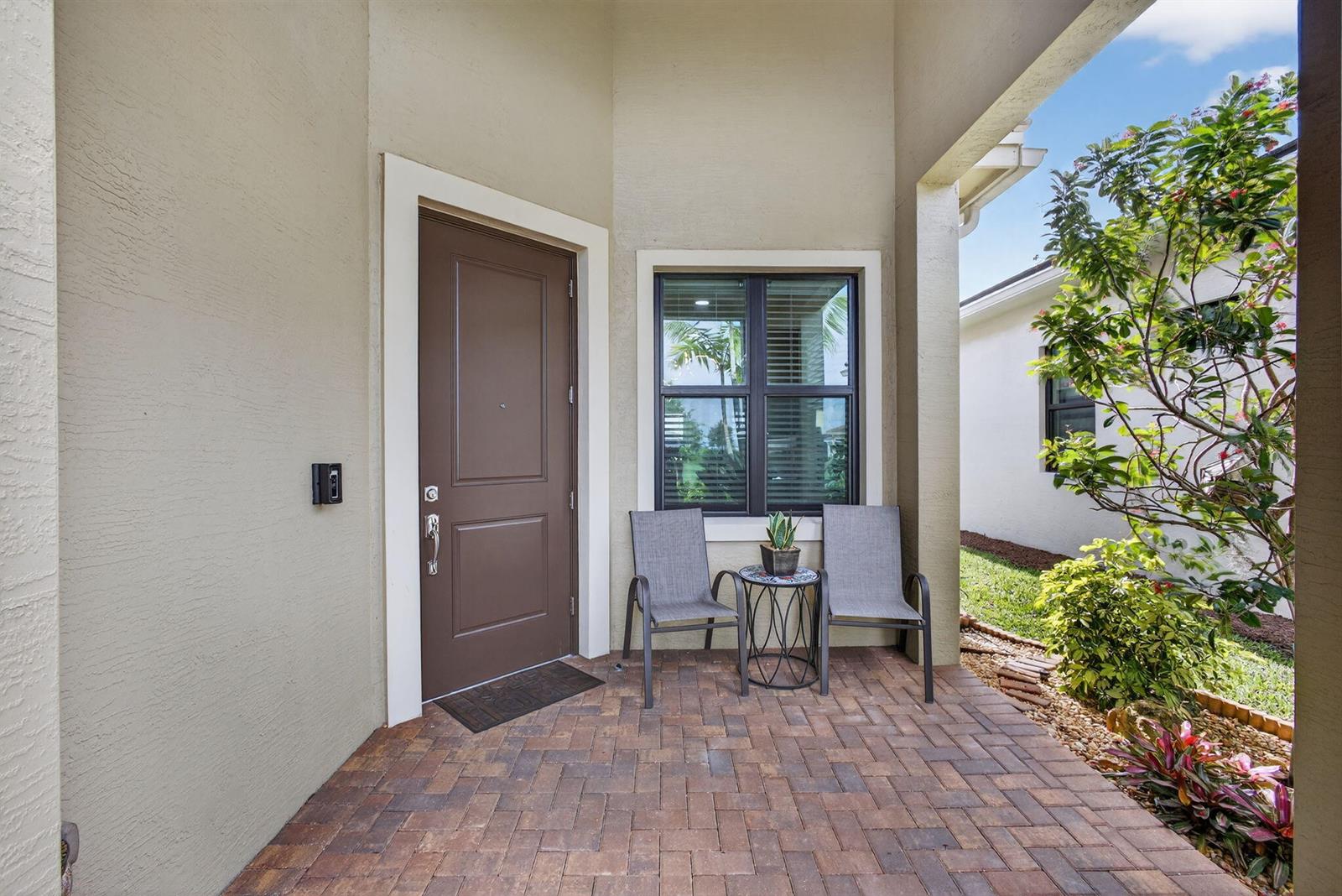 A brown front door and a window with two chairs sit on a brick porch — 4805 Saint Armands Way, Westlake FL 33470, WESTLAKE, FL