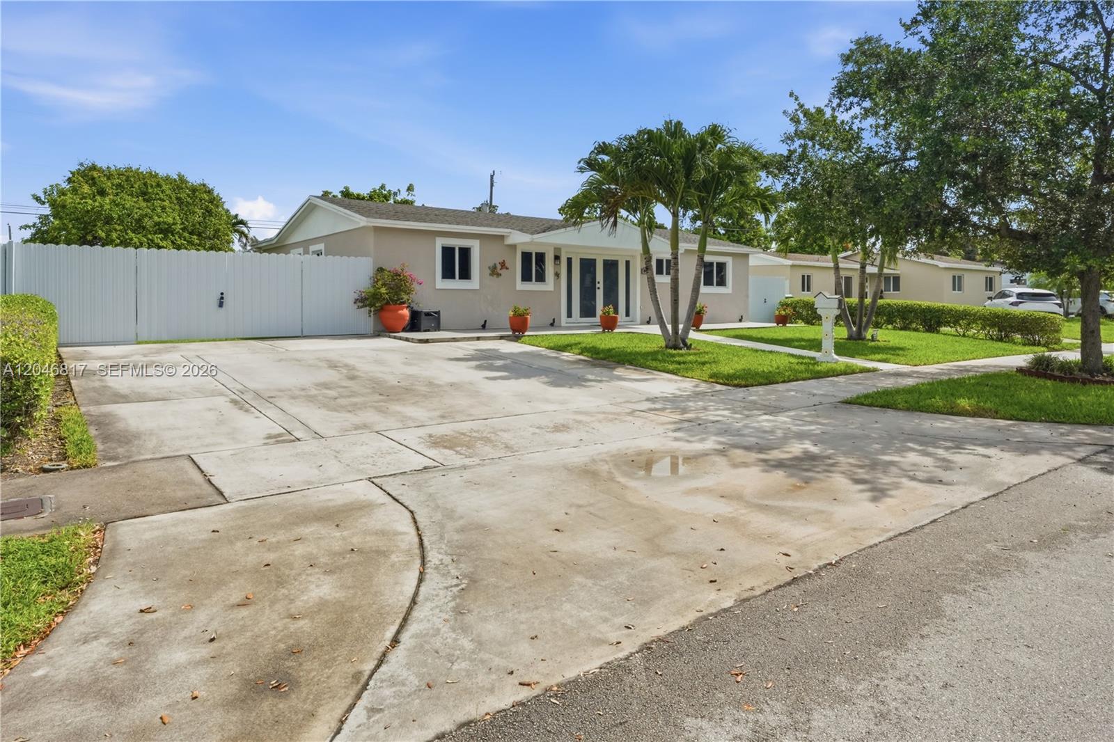 A single-story house features a large concrete driveway, a white fence, and palm trees — 10451 SW 201st Ter, Cutler Bay FL 33189, CUTLER BAY, FL