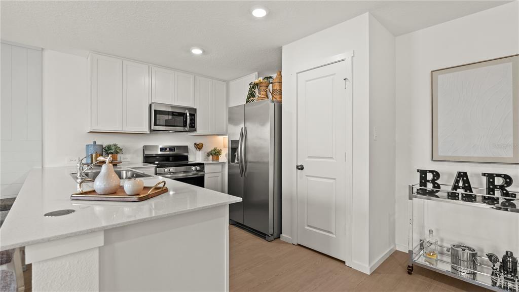 A modern kitchen features white cabinetry, stainless steel appliances, a quartz island, and a bar cart — 559 ARTEMIS STREET, LAKE WALES, FL