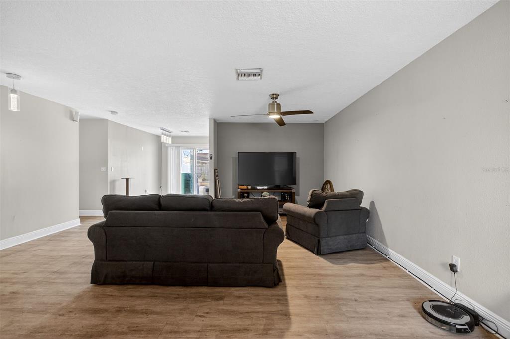 A living room features light wood-look flooring, gray walls, a ceiling fan, and dark furniture — 2738 FIRESIDE COURT, ORLANDO, FL