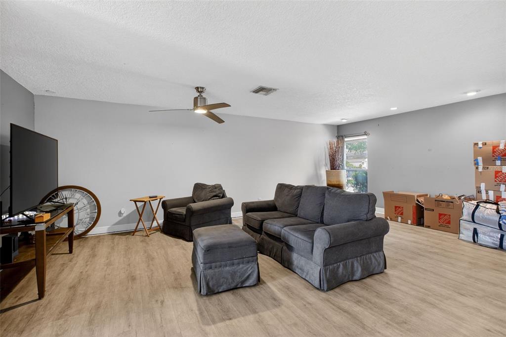 A living room features light wood-look flooring, gray furniture, a ceiling fan, and moving boxes — 2738 FIRESIDE COURT, ORLANDO, FL