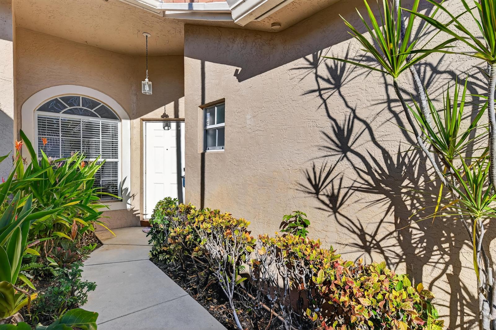 A beige stucco house exterior features a front door, arched window, and landscaped walkway — 6140 Long Key Lane, Boynton Beach FL 33472, BOYNTON BEACH, FL