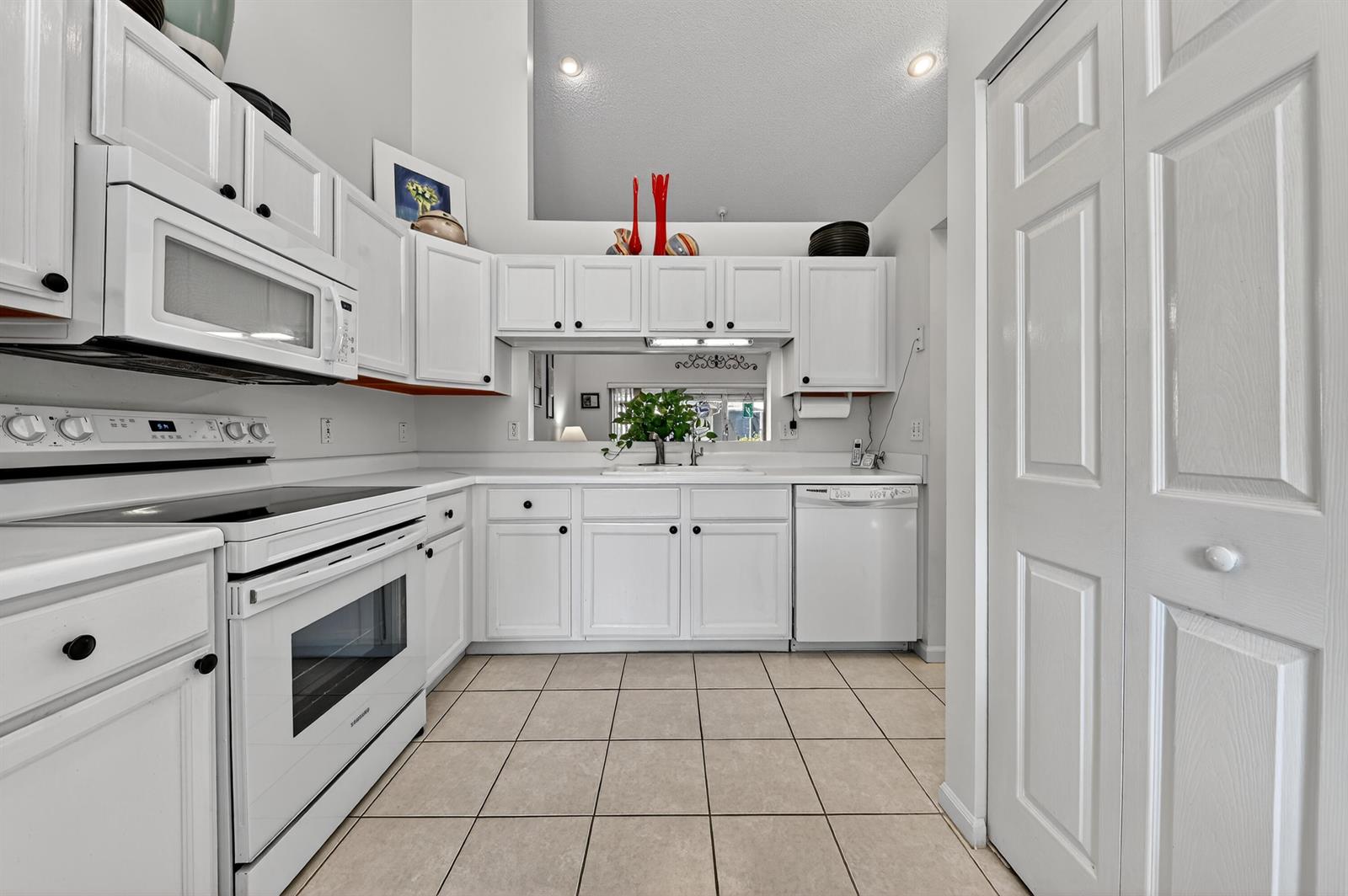A white kitchen features tile flooring, white cabinetry, and a pass-through window to another room — 6140 Long Key Lane, Boynton Beach FL 33472, BOYNTON BEACH, FL