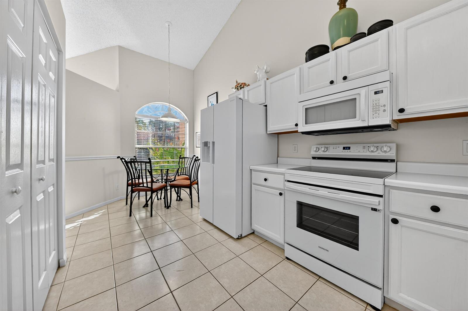 A kitchen with white cabinets and appliances features a dining area with a vaulted ceiling — 6140 Long Key Lane, Boynton Beach FL 33472, BOYNTON BEACH, FL