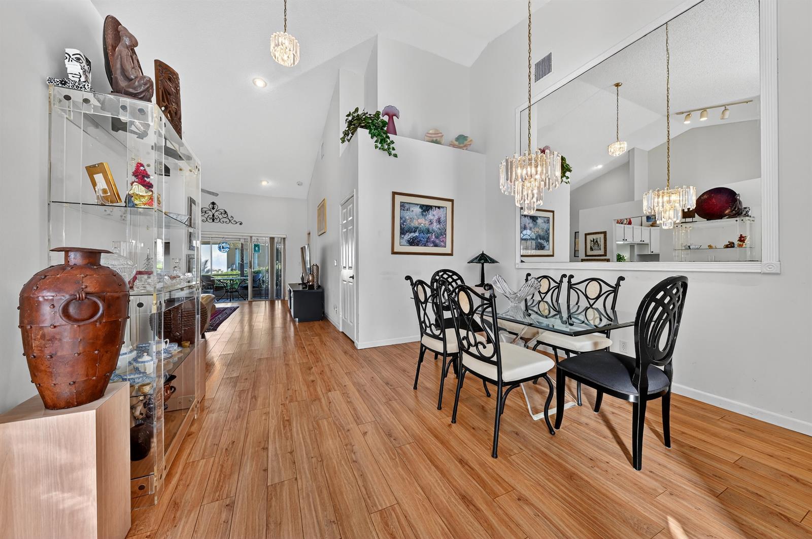 A dining area features a glass table, black chairs, crystal chandeliers, and wood-look flooring — 6140 Long Key Lane, Boynton Beach FL 33472, BOYNTON BEACH, FL
