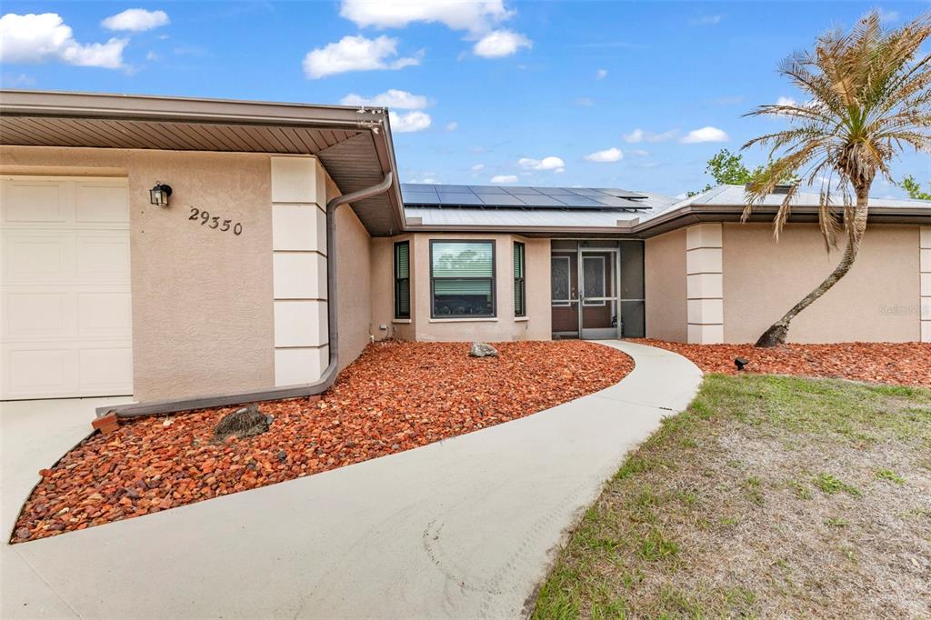 A single-story house with a tan stucco exterior, solar panels, and a curved concrete walkway — 29350 SAM WAY, PUNTA GORDA, FL