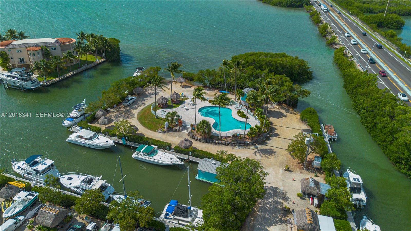 An aerial view shows a swimming pool surrounded by palm trees, docks, and parked boats — 100 Morr Ln C13, Key Largo FL 33037, KEY LARGO, FL