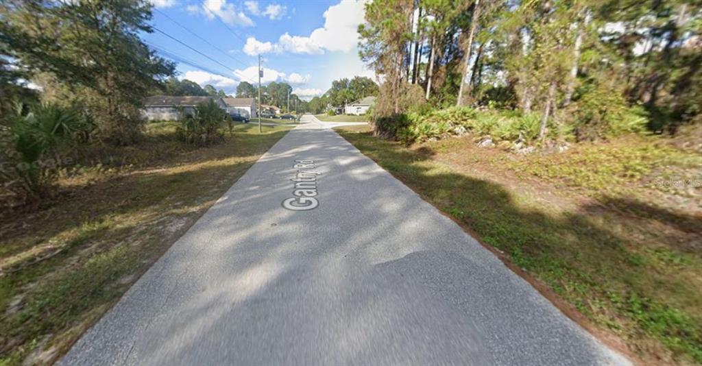 A paved road stretches through a wooded residential area under a blue sky — GANTRY ROAD, NORTH PORT, FL