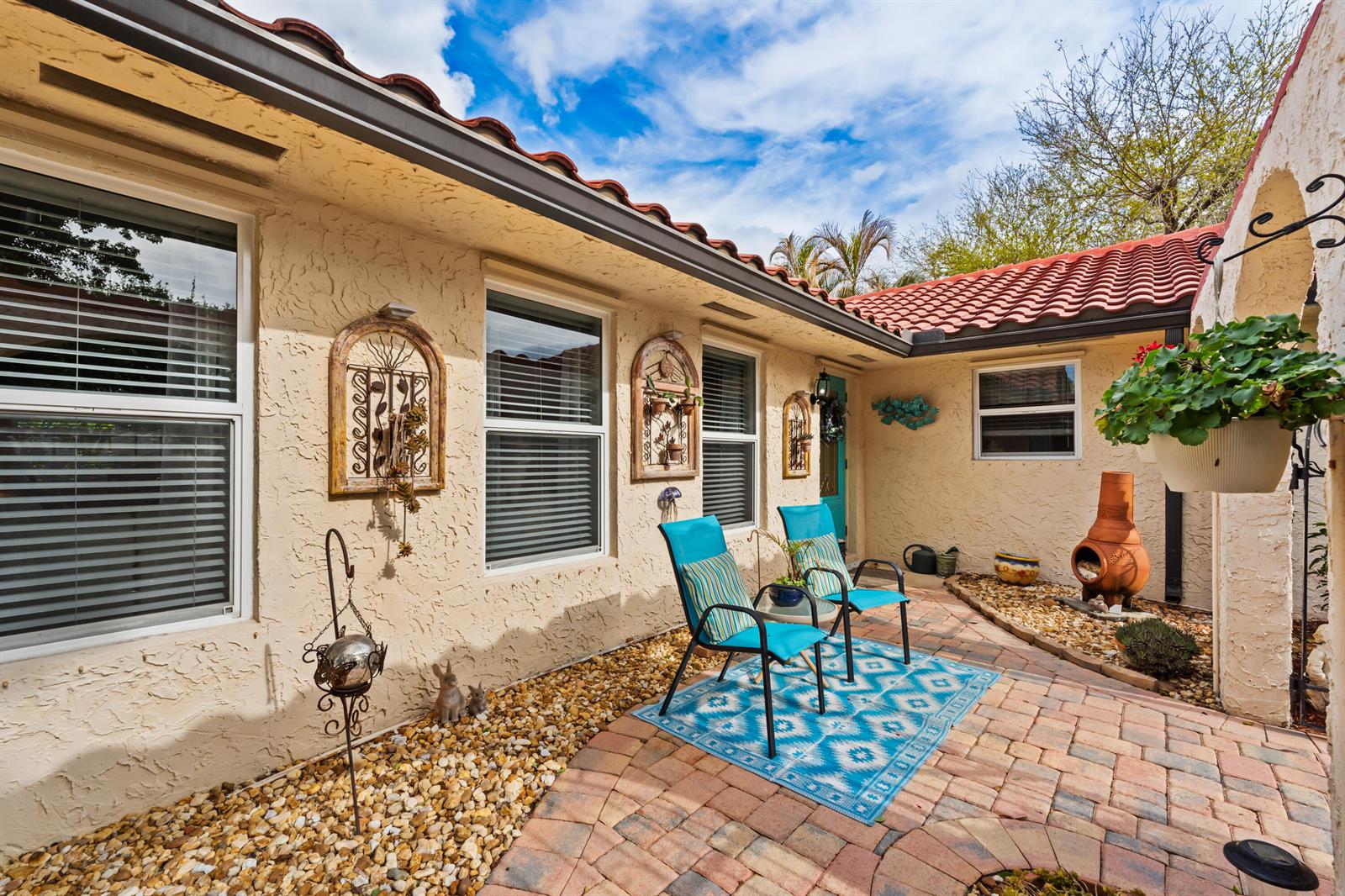 A patio with brick pavers, two blue chairs, and a rug sits against a stucco house — 4176 SE Fairway Court, Stuart FL 34997, STUART, FL