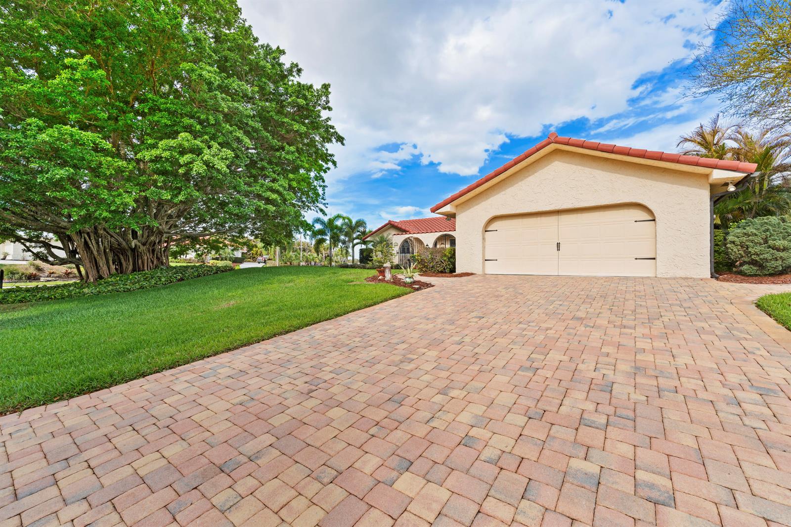 A paved driveway leads to a one-car garage in front of a house with trees — 4176 SE Fairway Court, Stuart FL 34997, STUART, FL