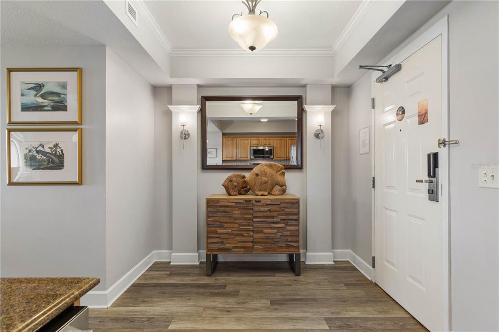 A foyer features wood-look flooring, a wooden cabinet, a mirror, and two framed bird prints — 200 OCEAN CREST DRIVE UNIT 617, PALM COAST, FL