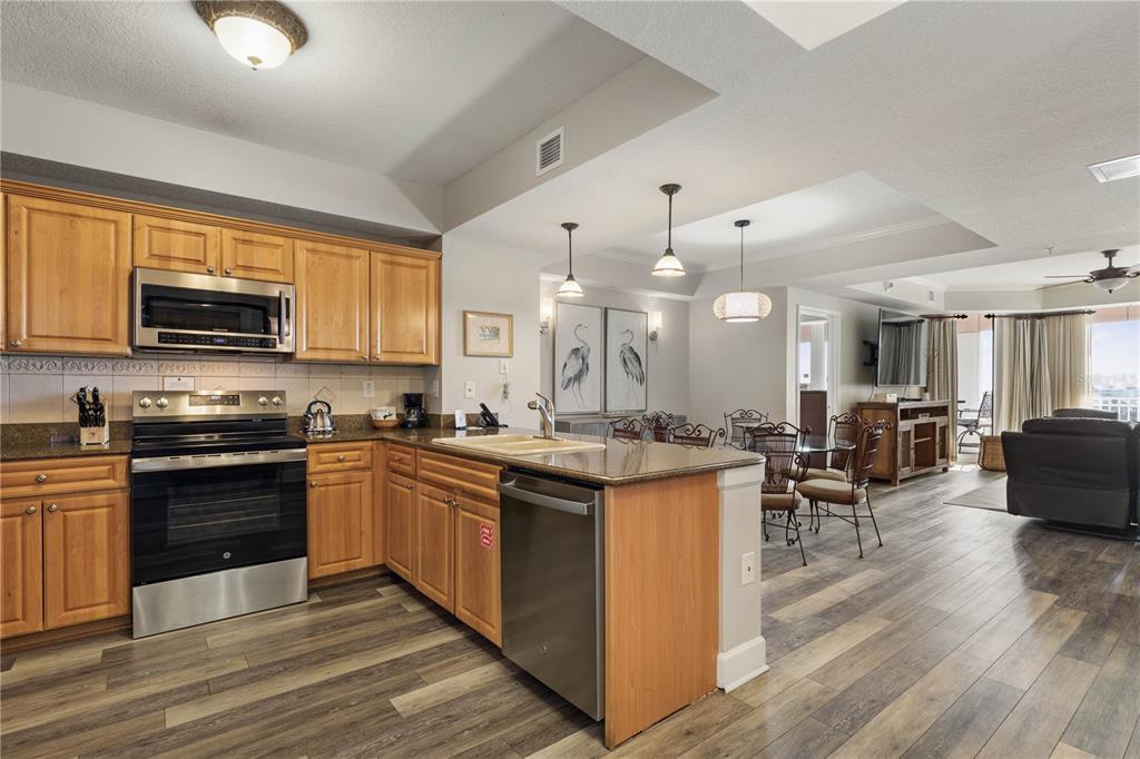 A kitchen with wood cabinets, stainless steel appliances, and granite countertops opens to a dining area — 200 OCEAN CREST DRIVE UNIT 617, PALM COAST, FL