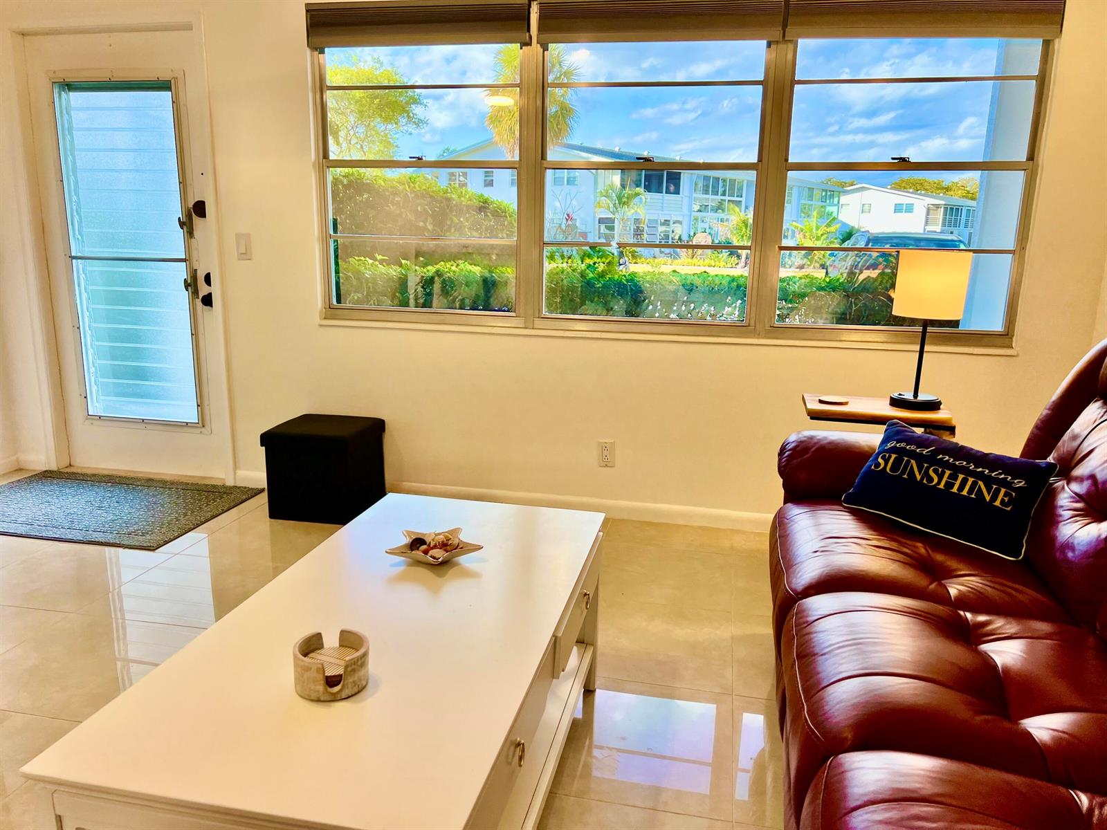 A living room features a red leather sofa, white coffee table, and large windows — 1011 Harwood C # 1011, Deerfield Beach FL 33442, DEERFIELD BEACH, FL